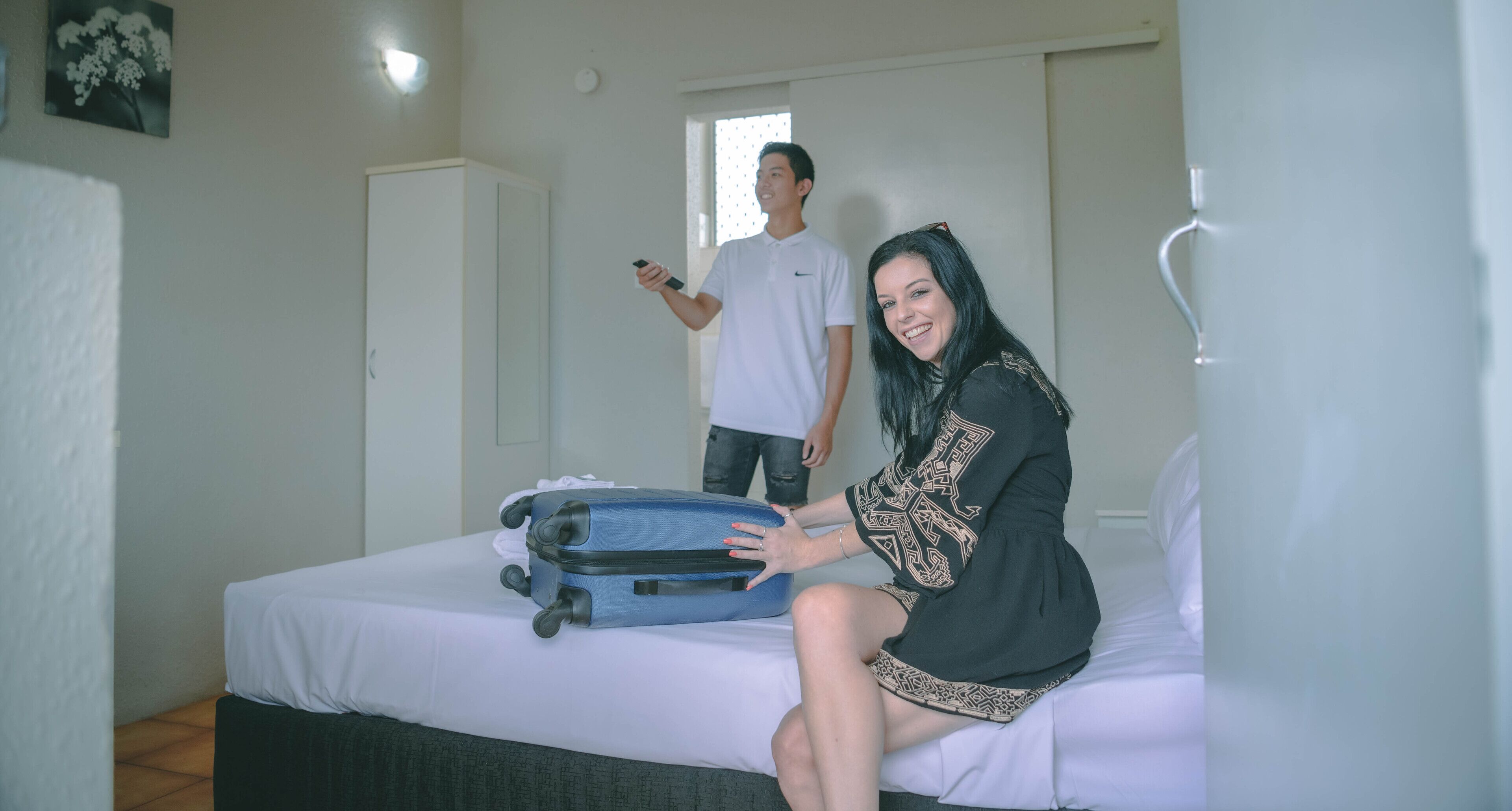 Una habitación de hotel con una cama, una maleta y una persona de fondo.