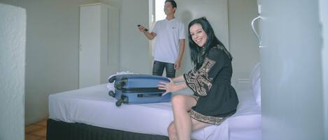 Una habitación de hotel con una cama, una maleta y una persona de fondo.