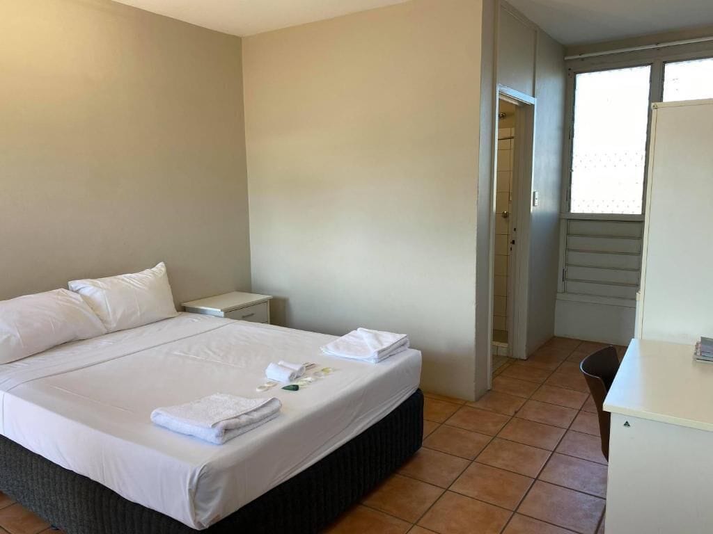 Una habitación de hotel con una cama, una mesita de noche, un escritorio y la puerta del baño.