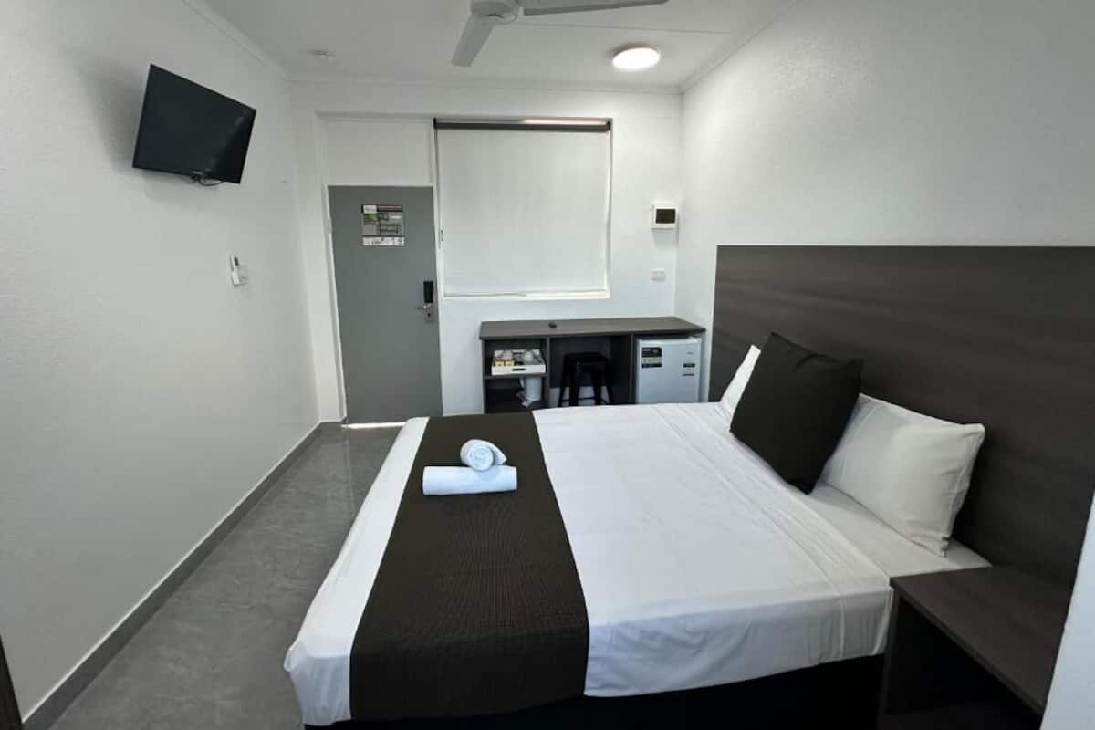 A hotel room with a bed, a desk, a chair, a TV, and a ceiling fan.