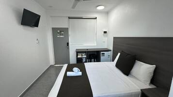 A hotel room with a bed, a desk, a chair, a TV, and a ceiling fan.