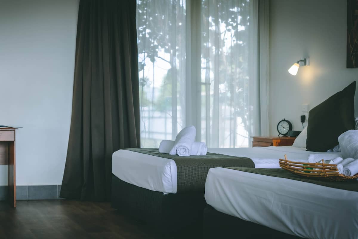 A hotel room with two beds, a desk, a chair, and a window with curtains.