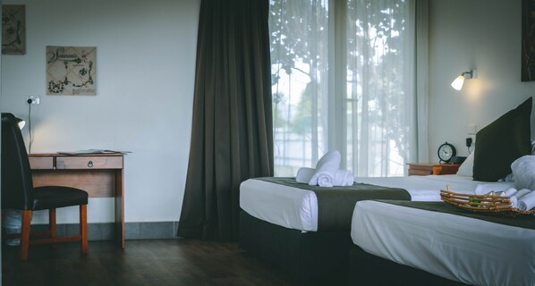 A hotel room with two beds, a desk, a chair, and a window with curtains.