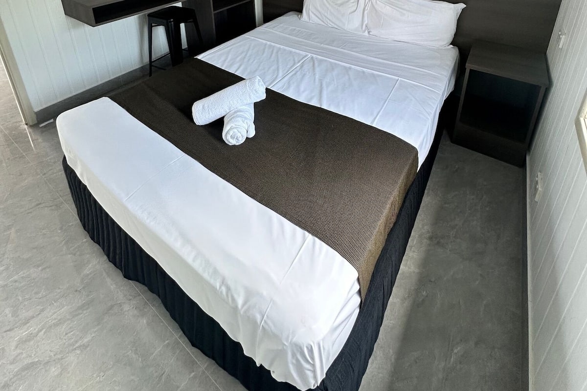 A hotel room with a large bed, a bedside table, a wardrobe, and a small desk.