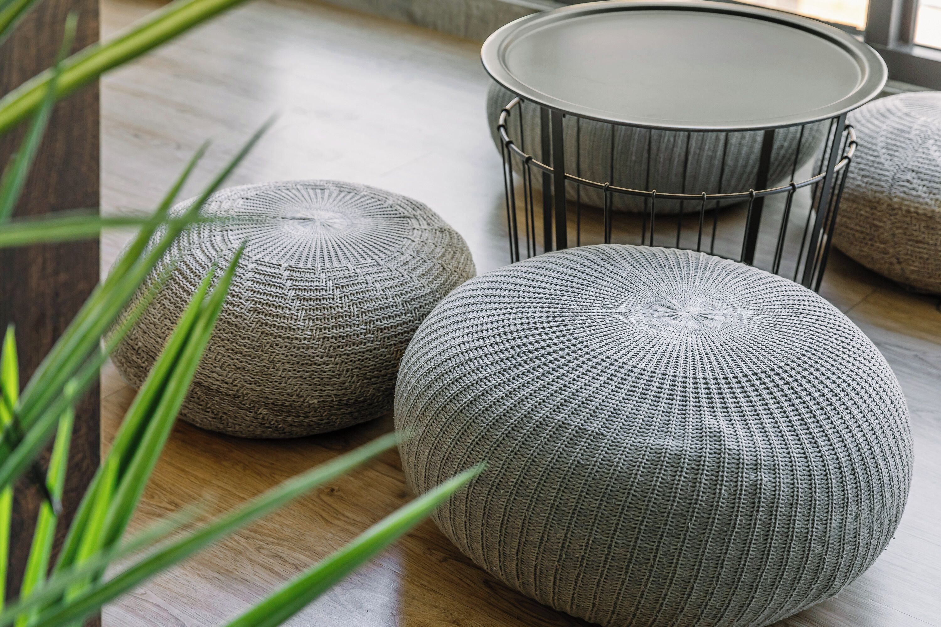Two round, textured ottomans and a metal-framed table on a wooden floor.