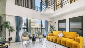A modern living room with a yellow sofa, a round coffee table, and two armchairs. There is a large window with curtains, a potted plant, and a TV on a stand. - Nan Nan (Kaohsiung)