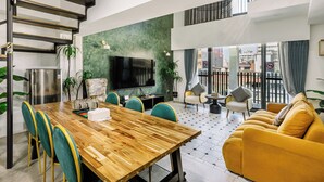 A spacious living area with a wooden dining table, teal chairs, a yellow sofa, and a staircase. - Nan Nan (Kaohsiung)