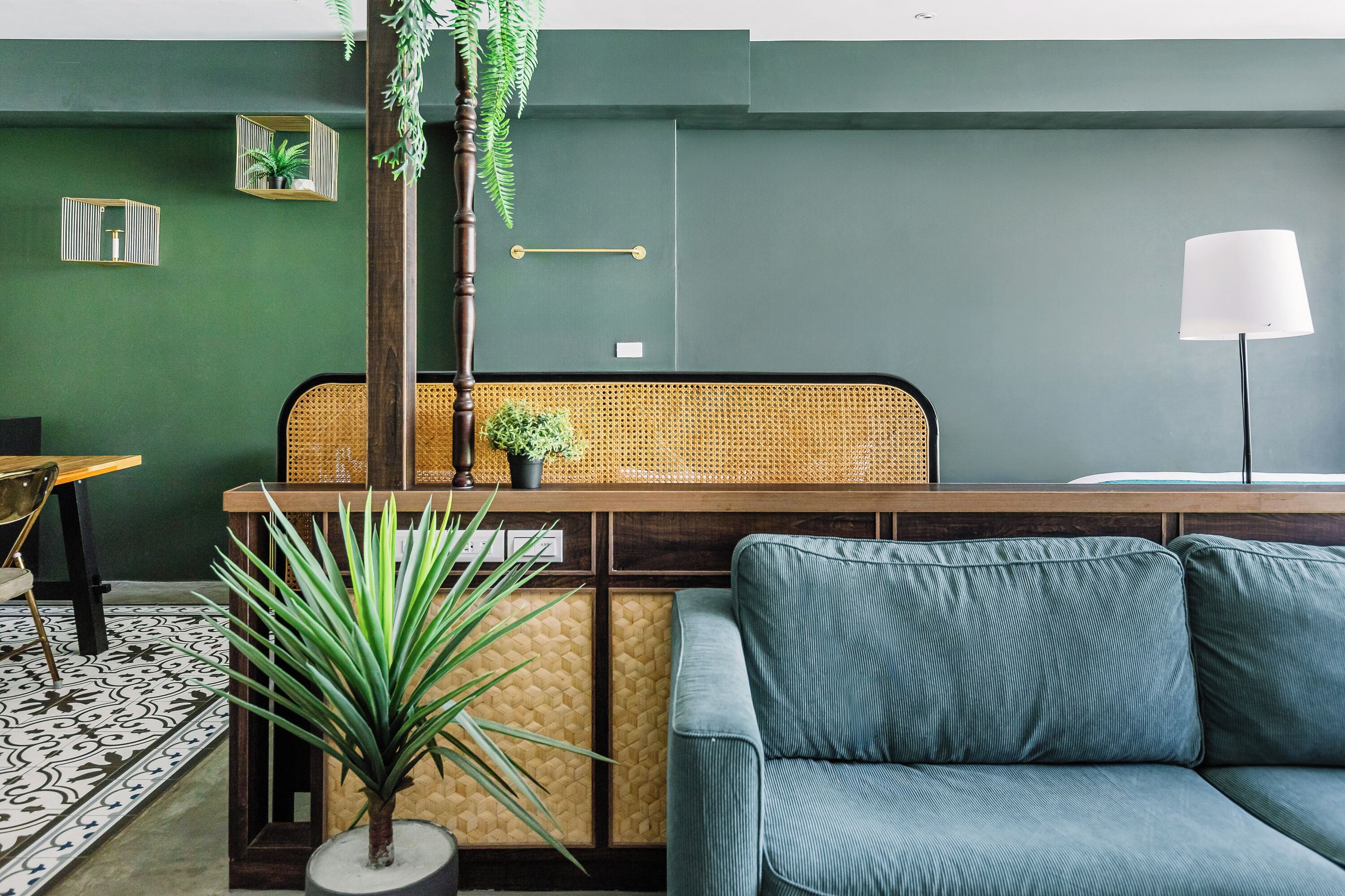 A modern living room with a green wall, a blue sofa, a wooden coffee table, a wicker chair, and a floor lamp.