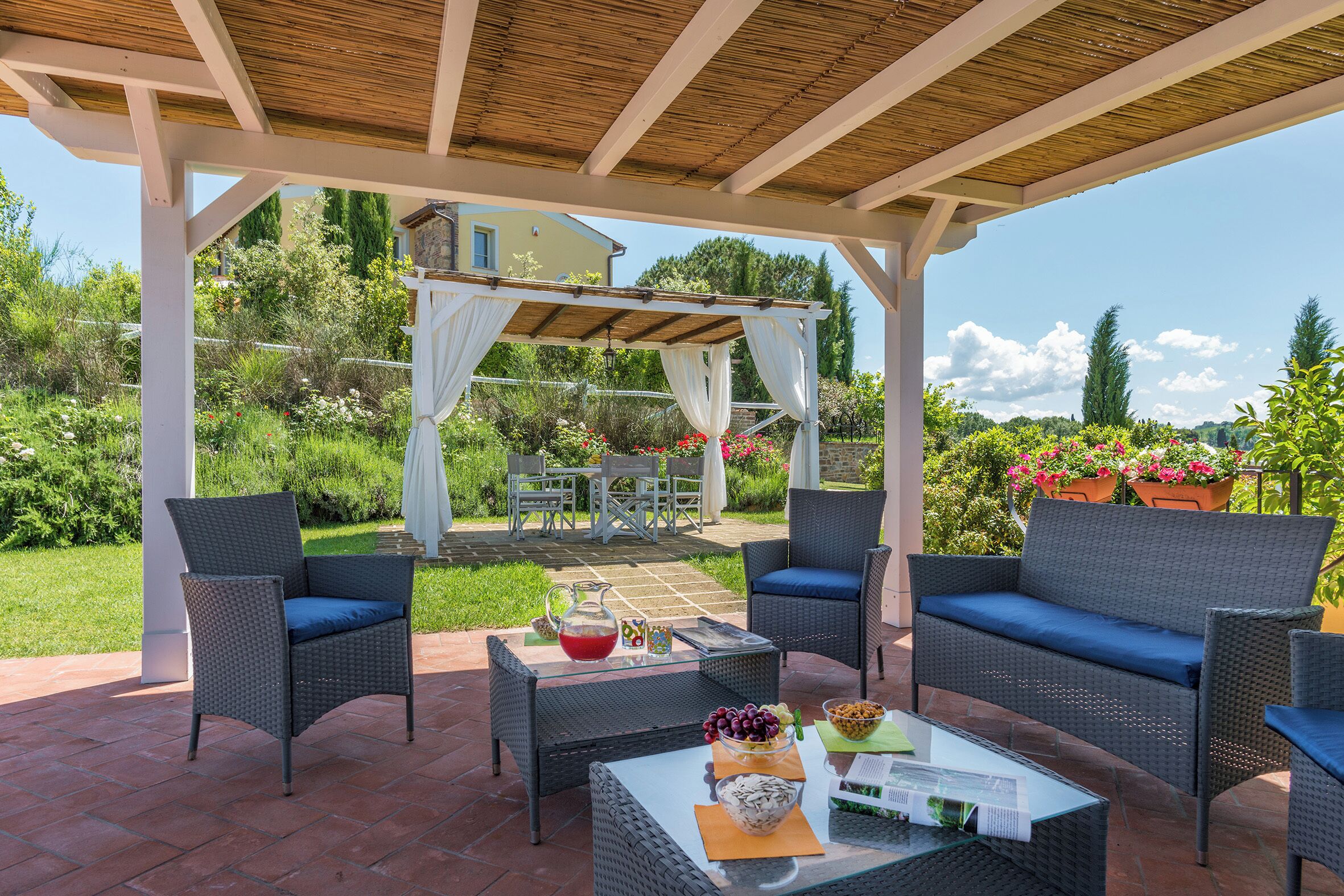An outdoor patio with wicker furniture, a glass table, and a pergola structure.
