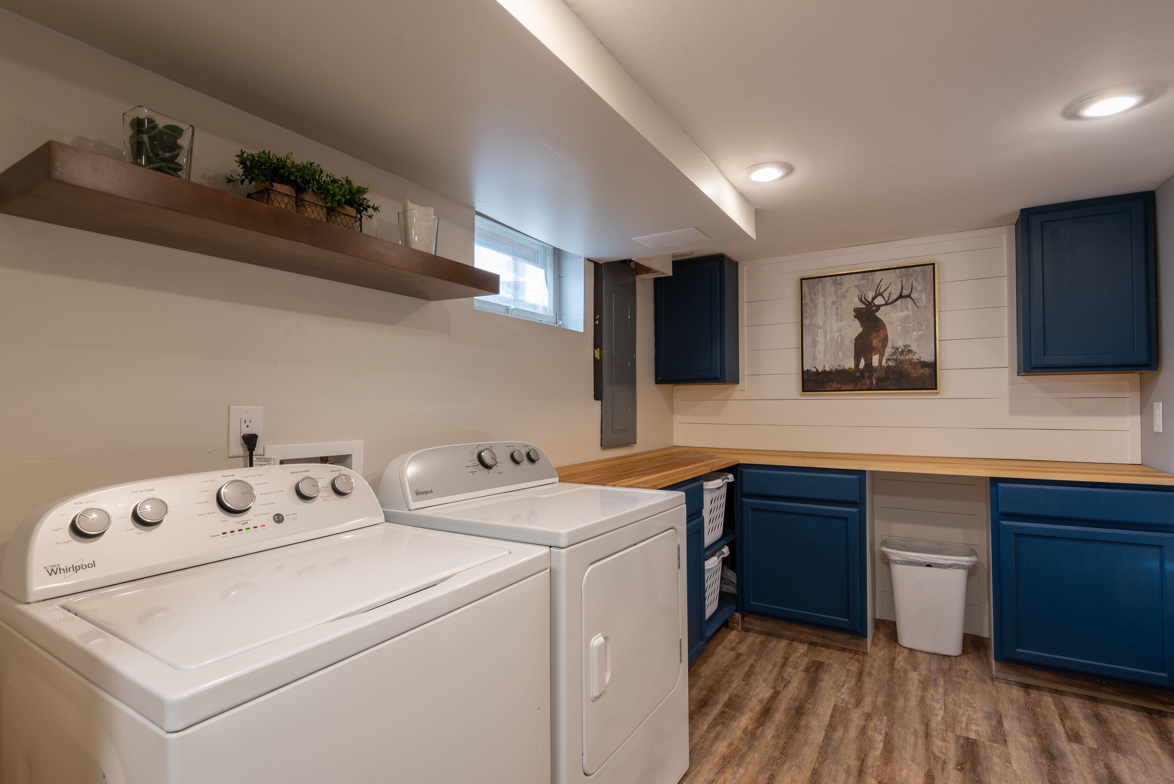 A laundry area with two Whirlpool washers, a wooden countertop, and a blue cabinet.
