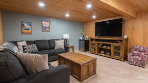 Un accogliente soggiorno con un divano scuro, un tavolino in legno, una TV a schermo piatto e un mobile contenitore con scaffali.