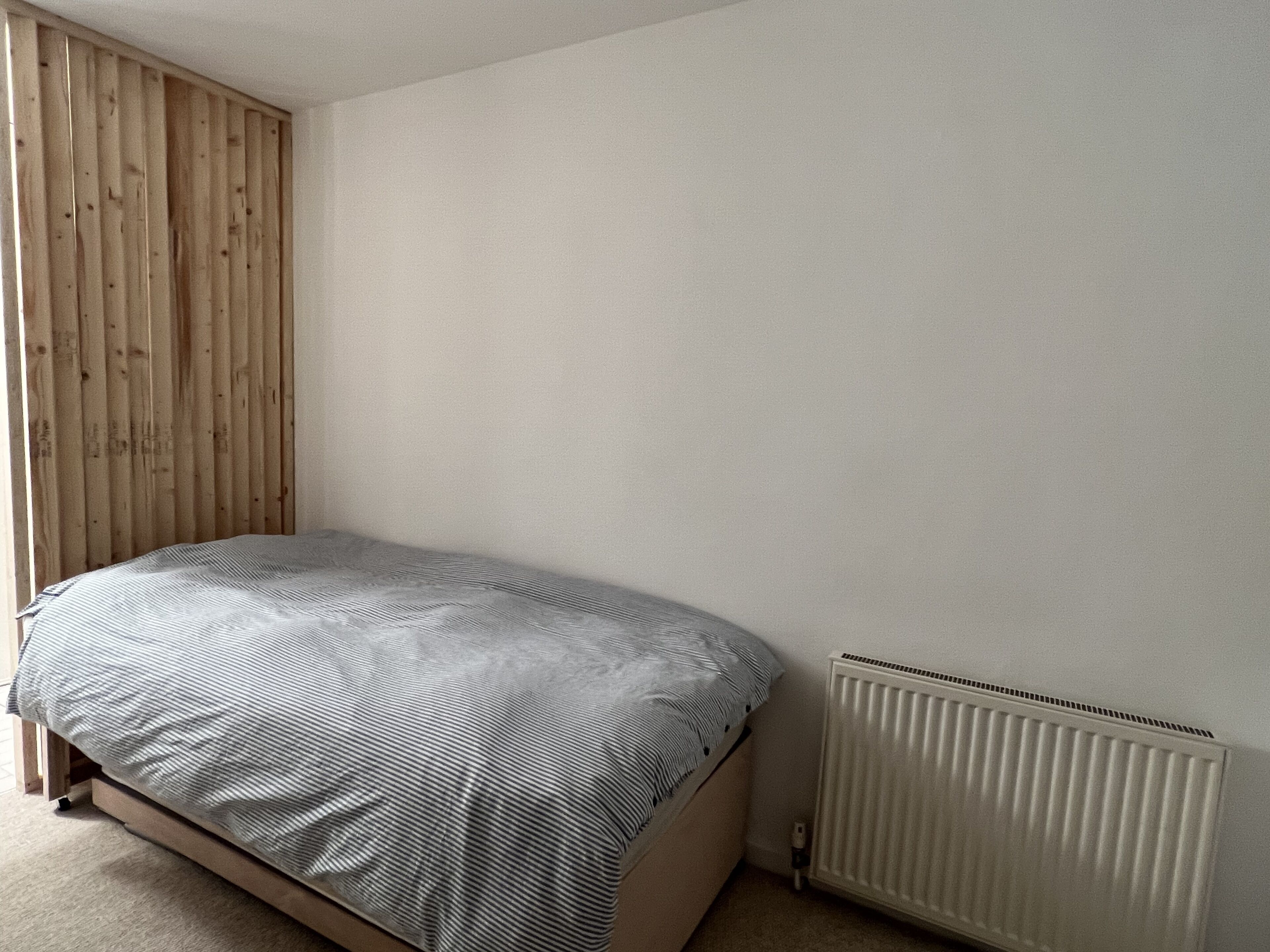 Een slaapkamer met een bed, een houten garderobe en een radiator.