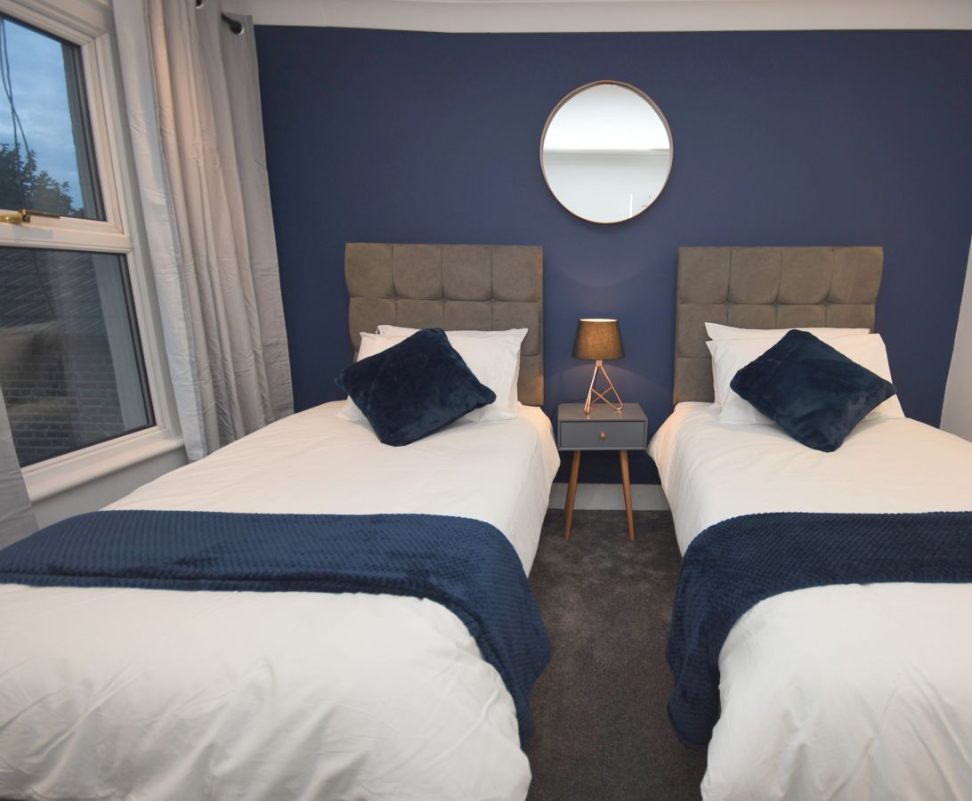 Une chambre double avec deux lits, un miroir rond, une table de chevet avec une lampe et une vue sur l’extérieur.