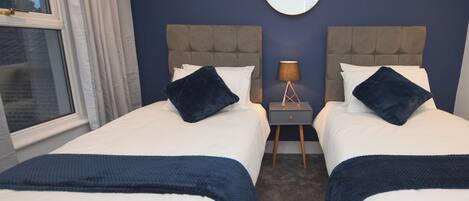 A double room with two beds, a round mirror, a nightstand with a lamp, and a view of the outside.
