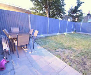 A backyard with a patio table and chairs, a blue fence, and a grassy lawn.