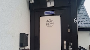 Una puerta con marco negro, panel blanco y un letrero con el número 6, además de un cartel de bienvenida sobre la puerta.