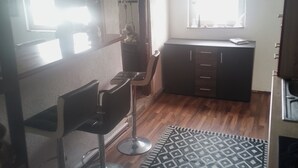 Una habitación con barra, ventana con cortinas, alfombra estampada y kitchenette.
