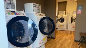 A laundry facility with multiple washing machines and dryers, wooden flooring, and safety signs. - HOTEL R9 The Yard Inabe (Inabe)