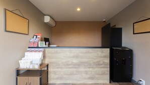 A reception area with a wooden reception desk, a bulletin board, a black safe, and a small cabinet with brochures. - HOTEL R9 The Yard Inabe (Inabe)