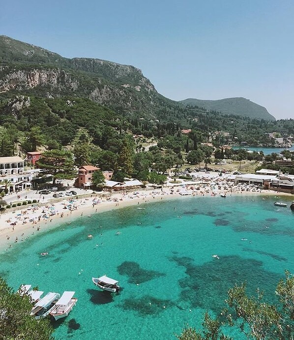 A coastal town with a beach, boats, and mountainous backdrop.