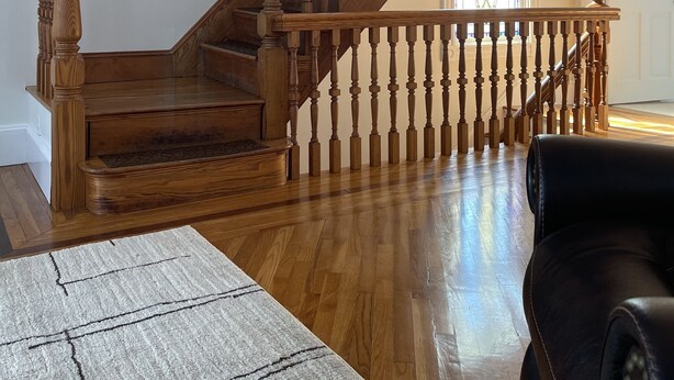 Una escalera de madera con barandilla, una ventana con marco blanco y una alfombra estampada sobre piso de madera.