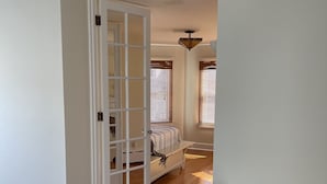 Una habitación con suelo de madera, cama con colcha a rayas y ventana con persianas.