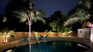 A nighttime swimming pool area with lounge chairs and palm trees.
