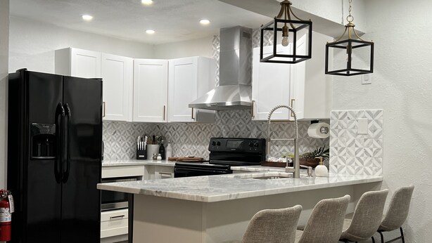 A modern kitchen with white cabinets, a black refrigerator, a central island with bar stools, and pendant lighting.