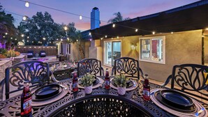 Un patio al aire libre con una mesa lista para comer, rodeada de sillas y luces colgantes.