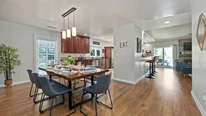 Una cocina moderna con armarios de madera, una mesa de comedor preparada para cuatro personas y lámparas colgantes.