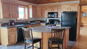 A spacious kitchen with wooden cabinets, a central island with chairs, a black refrigerator, and a microwave. - Large garage for bikes. Beautiful log home.  On golf course. (Hulett)