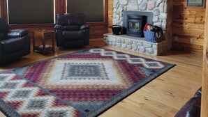 A log cabin interior with a stone fireplace, leather sofas, and a large window. - Large garage for bikes. Beautiful log home.  On golf course. (Hulett)