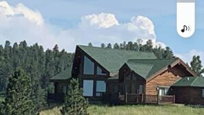 A cabin with a large window, surrounded by trees and a grassy field. - Large garage for bikes. Beautiful log home.  On golf course. (Hulett)
