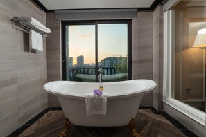 Une salle de bain moderne avec une baignoire sur pieds, une douche à parois de verre et une vue sur le paysage urbain, visible à travers une grande fenêtre.