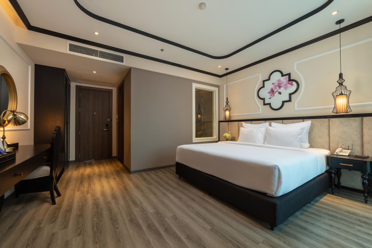 A modern hotel room with a large bed, a desk with a lamp, and a decorative wall piece.