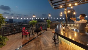 Een terras op een dak met uitzicht over de stad, houten vloeren en lichtjes.