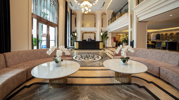 Een ruime lobby met een receptiebalie, twee banken en een kroonluchter.