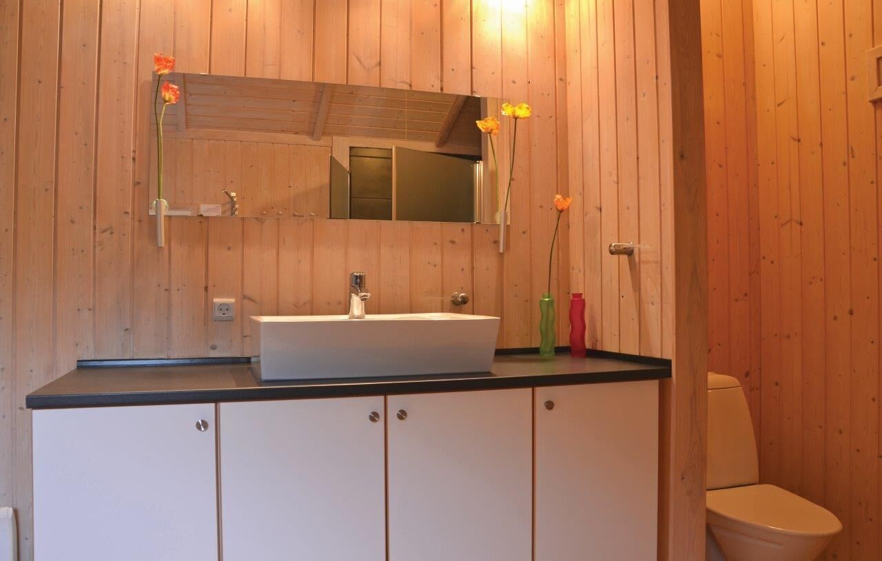 A bathroom with wooden walls, a white sink, a mirror, and a toilet.