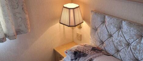 A bedroom with a bed, a nightstand, a lamp, and a wardrobe.