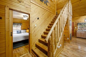 Ein Holzblockhaus-Interieur mit Treppe, einem Bett mit kariertem Schutz und einer Küchenzeile.