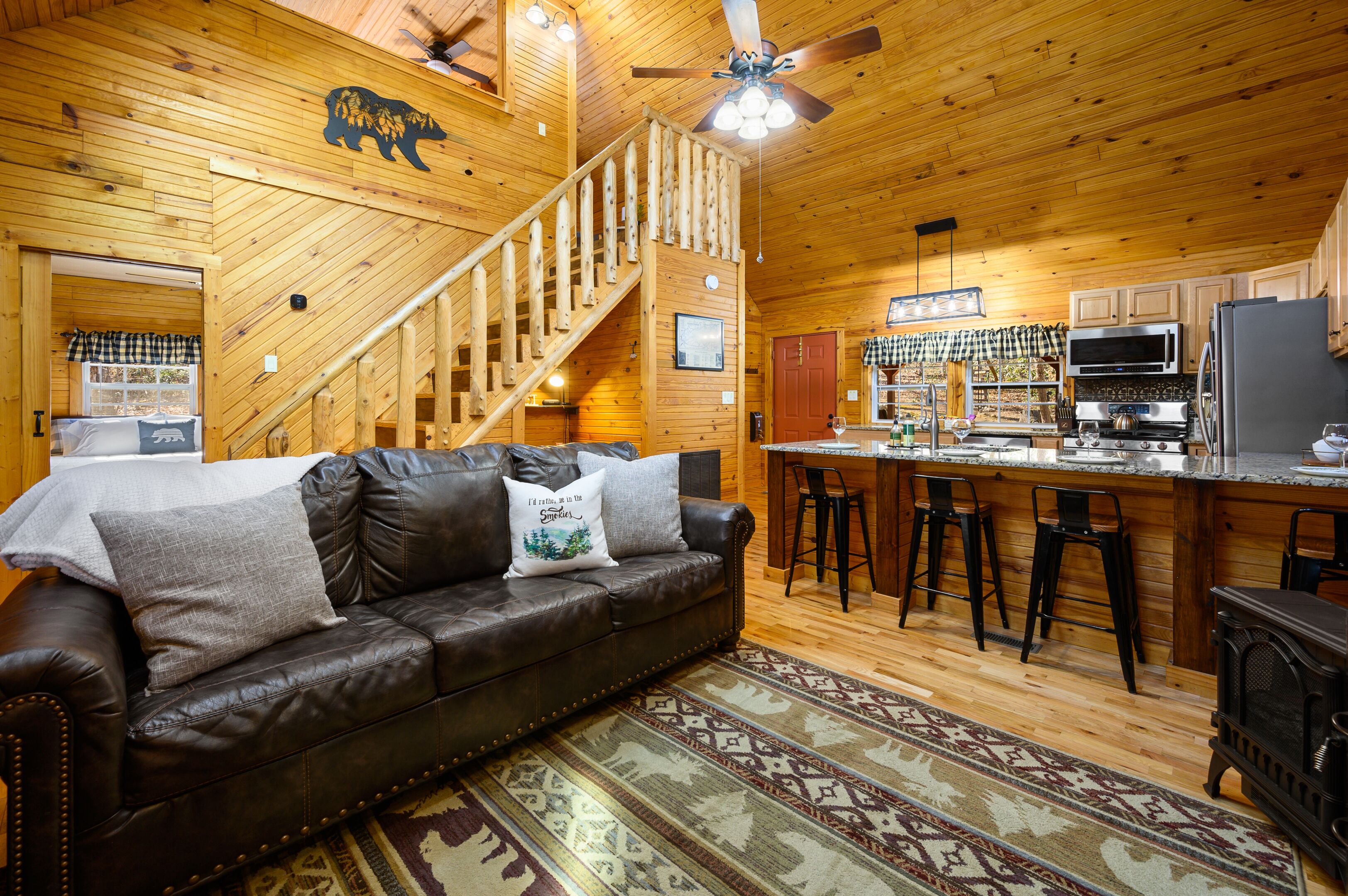 Ein Holzblockhaus-Interieur mit Ledersofa, Treppe, Küchenbereich und Bar.