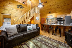 Ein Holzblockhaus-Interieur mit Ledersofa, Treppe, Küchenbereich und Bar.