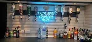 A bar area with a neon sign reading 'TWAIN AYE'S COUNTRY PARK' and various liquor bottles. - Glamping Hut - Riverview 3 (Welshpool)