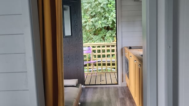Un pasillo estrecho que conduce a un balcón con terraza de madera y vistas al verdor, además de una zona de cocina con armarios de madera.