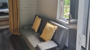 Un espacio habitable compacto con un sofá, dos cojines, un cuadro, una ventana y una cortina.
