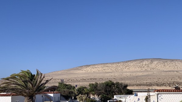 A desert landscape with a hill in the background, a clear blue sky, and some buildings in the foreground. - Stunning and modern holiday rental with sea view (Costa Calma (incl. Urbanización Cañada d)