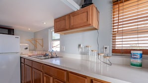 A modern kitchen with wooden cabinets, a white countertop, a built-in microwave, and a window with blinds. - Affordable, Private, Cozy Retreat-Tiny Cowboy Stay (Queen Creek)