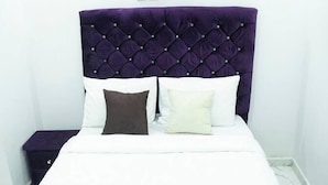 A neatly made bed with a tufted headboard, white bedding, and two pillows. - Charming 1-Bed Apartment in Abuja (Abuja)