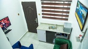 A compact room with a kitchenette, a TV, a bed, and a window with blinds. - Charming 1-Bed Apartment in Abuja (Abuja)