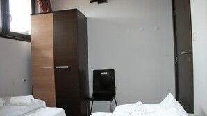 Una habitación de hotel con dos camas, un armario, una silla y una ventana.